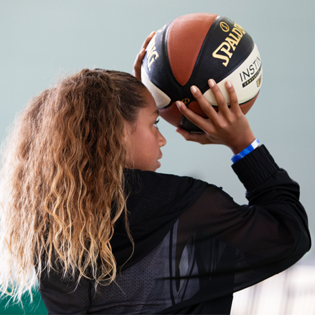Female model shooting Instinct TF basketball wearing a black jacket. 